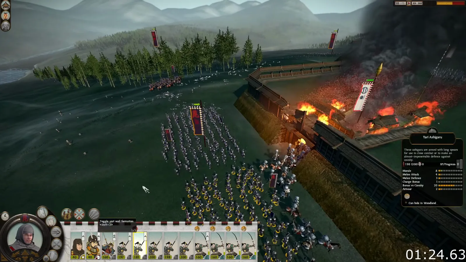 Infantry assault a burning gate in classic Shogun 2 while supporting troops wait outside the castle wall.